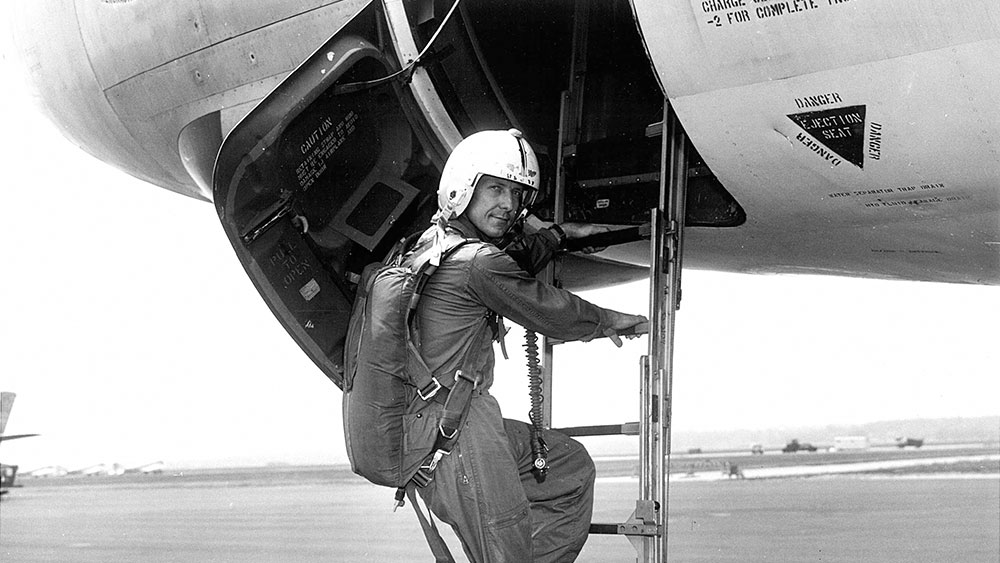 Black and white photo of a male pilot climbing aboard a plane.