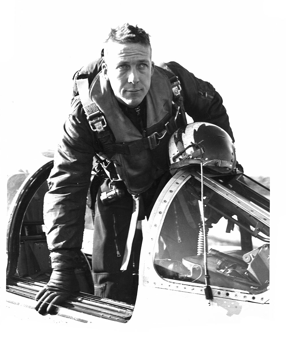 Black and white photo of a young pilot stepping out of the cockpit of an aircraft.