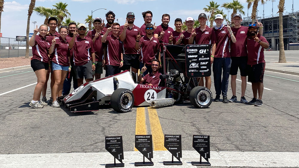 Team standing behind car and trophies 