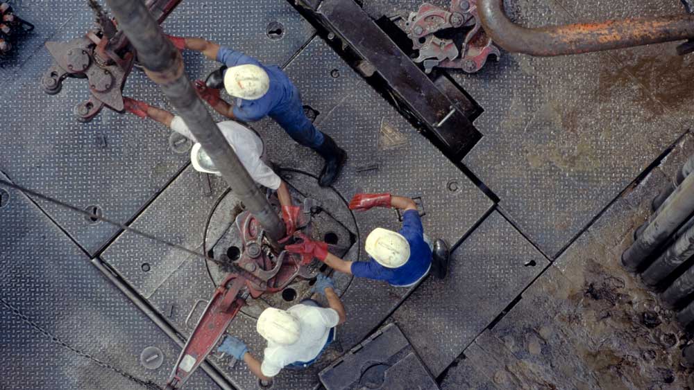 Overhead view of four workers wearing hardhats using equipment on a drilling rig