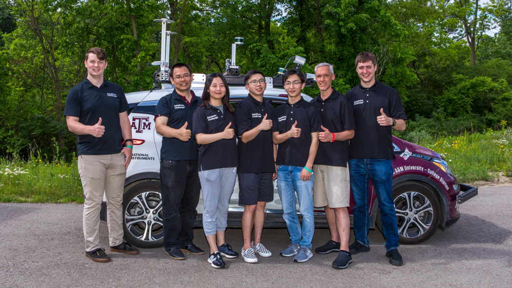 Five members of the Texas A&amp;M 12th Unmanned Team and two of their advisors standing in front of their maroon and white autonomous car. They are all smiling and giving the gig 'em hand sign.