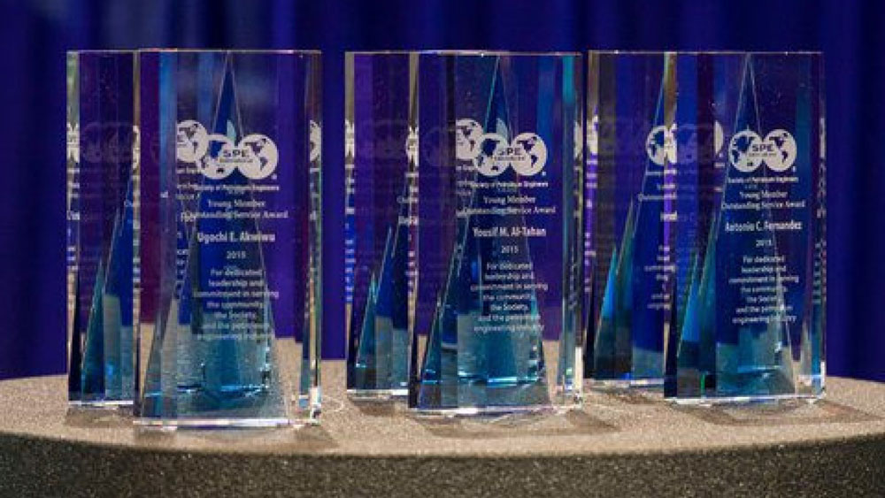several glass awards adorned with Society of Petroleum Engineers logos arranged on a tabletop