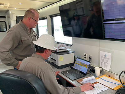 two men in a trailer on a fracturing site studying complex readouts on computer screens