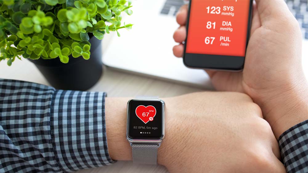 A person wearing a device that monitors heart rate while looking at a phone screen with more information on blood pressure