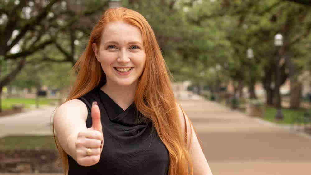 Emer Phelan smiling and giving a thumb's up outdoors on the Texas A&M University campus