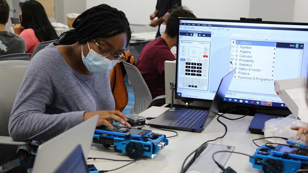 Girl working on calculator rover next to monitor.