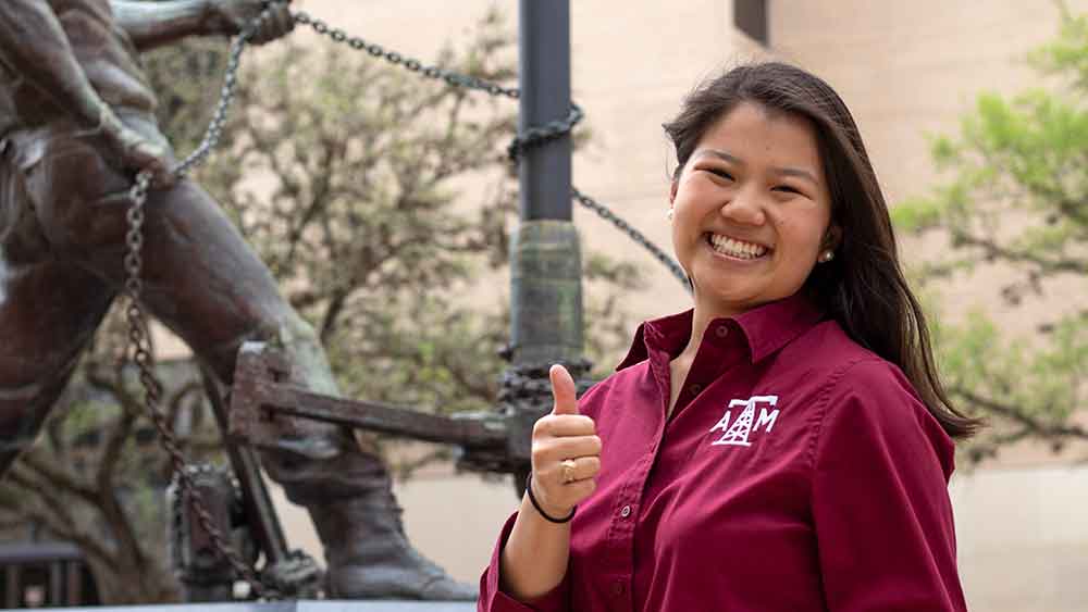 Female petroleum engineering student smiling and giving a Texas A&M University thumbs up Aggie hand gesture