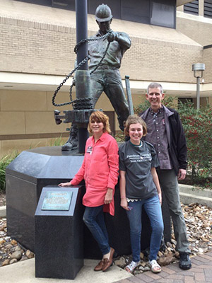 Female high-school student standing with parents next to statue of roughneck on Texas A&amp;M campus