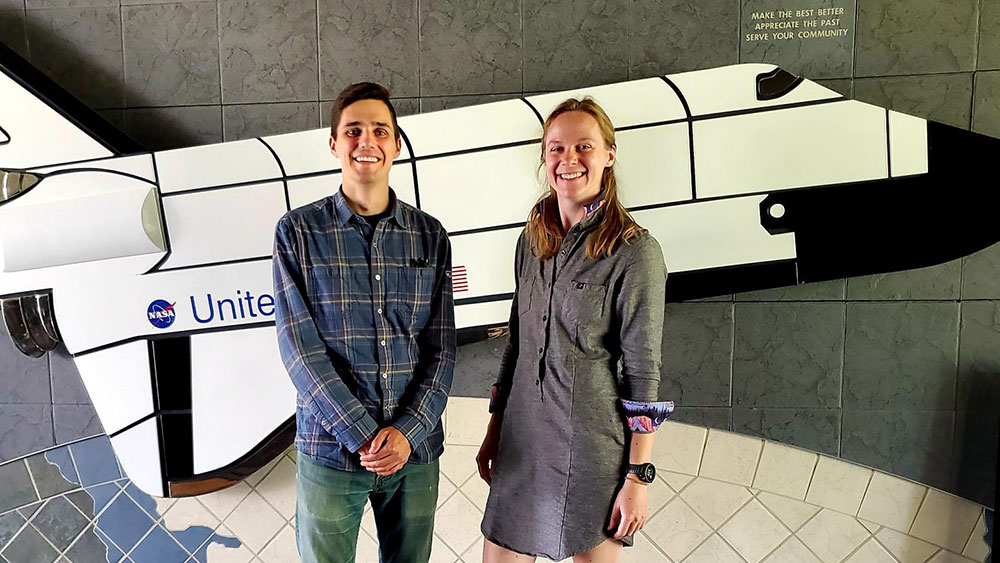 Patrick Walgren and Hannah Stroud posed for a photo in front of a decor piece of a NASA space shuttle.