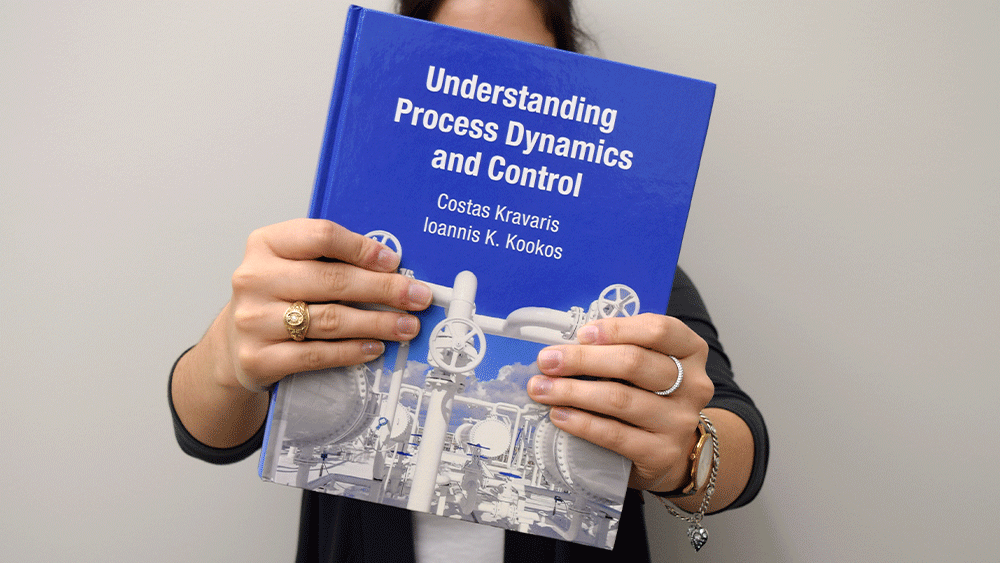 A woman holding the book Understanding Process Dynamics and Control by Costas Kravaris and Ioannis Kookos  in front of her face.