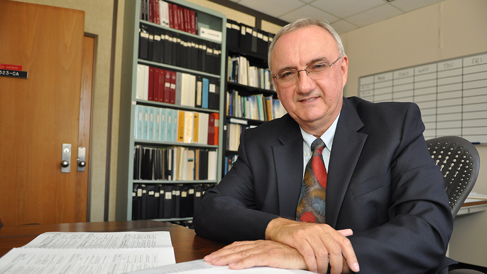 Dr.  Mladen Kezunovic sitting at his desk in his office with books behind him.