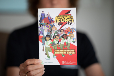 The cover a comic book. On it are drawings of animated students and inventors dressed as superheroes. The text reads "National Inventors Hall of Fame Innovation Force. The Hazardous Chemical Caper. Camp Invention, National Inventors Hall of Fame."