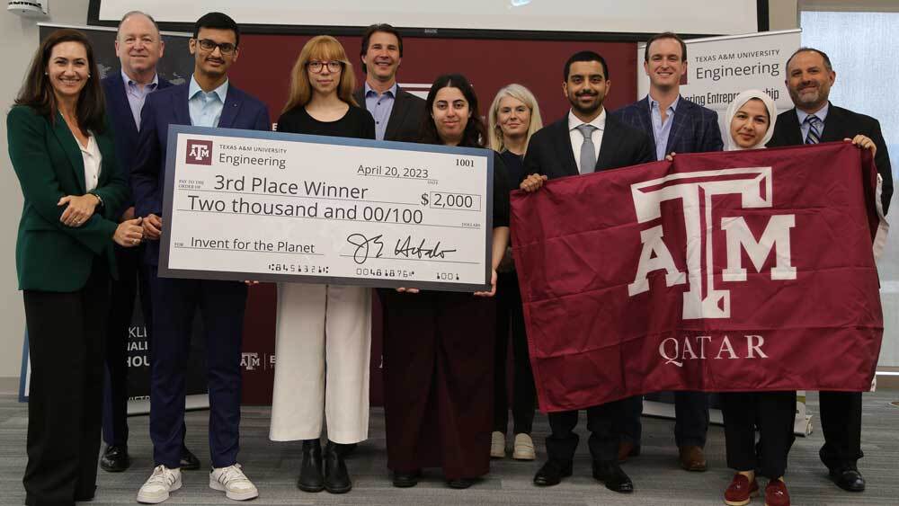 The third-place team from Texas A&amp;M University at Qatar with their university flag and an oversized $2,000 check.
