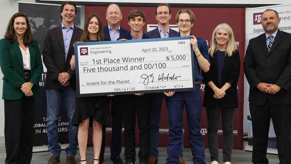 The first-place team from Swansea University in Wales, H2Grow, stands with judges and an oversized $5,000 check.
