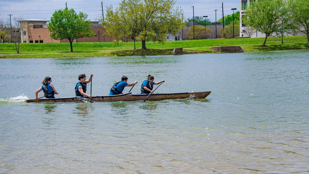 Four people paddle across a lake in a canoe