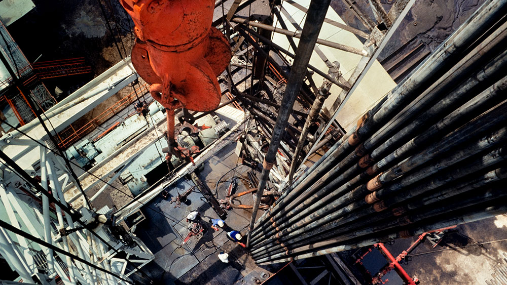 Four workers wearing hard hats on a drilling platform as seen from high above in the rig scaffolding
