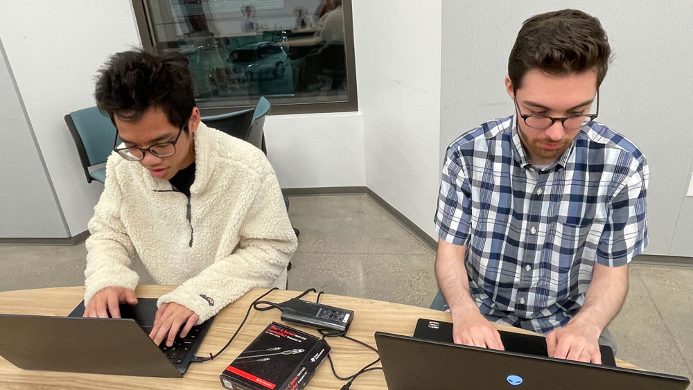 Two members of Texas A&amp;M University's embedded capture the flag team working on their laptops during a practice session.