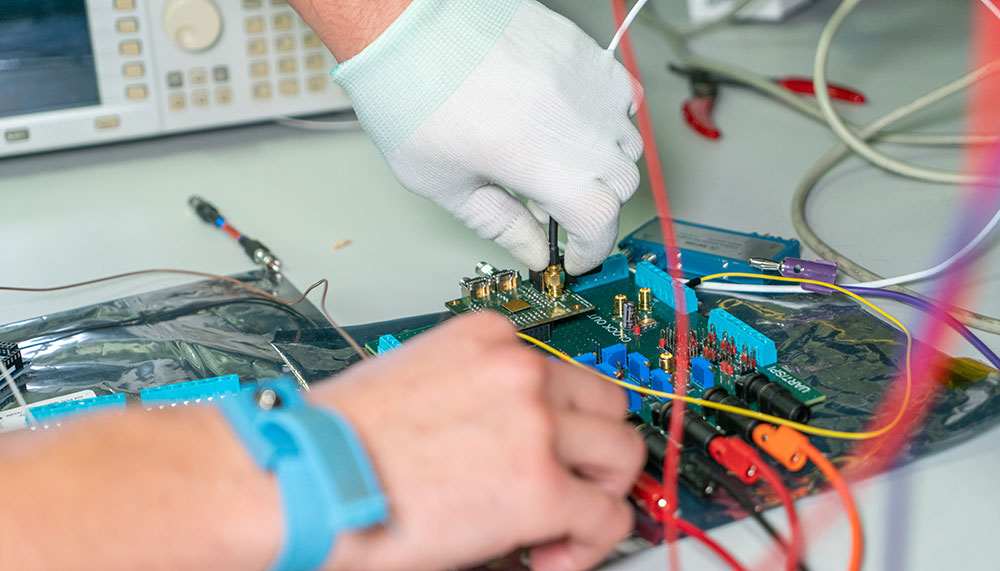 Hand with gloves holding wires connected to integrated circuit on a desk