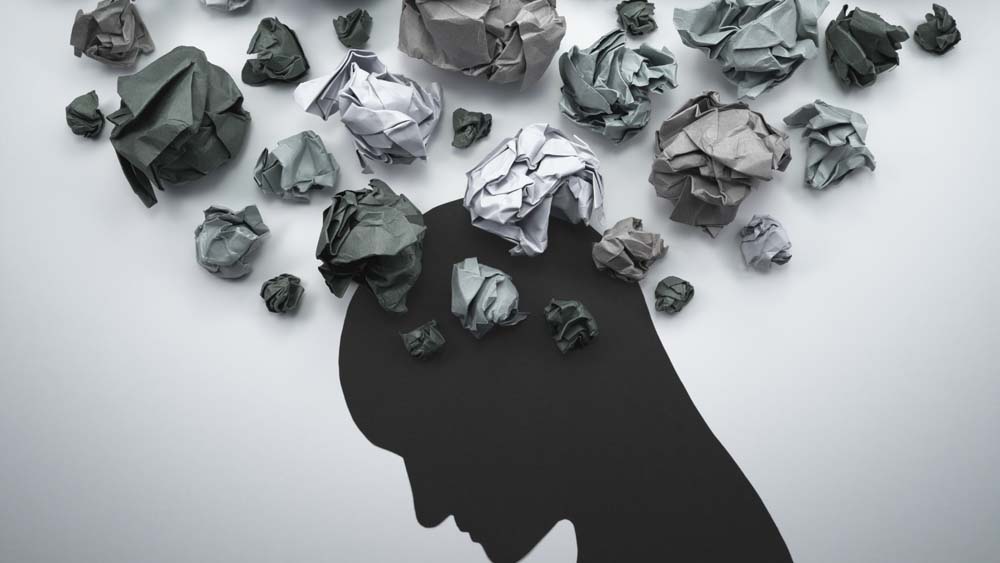 A silhouette of a person with their head bent. Above them are crumpled pieces of gray paper.