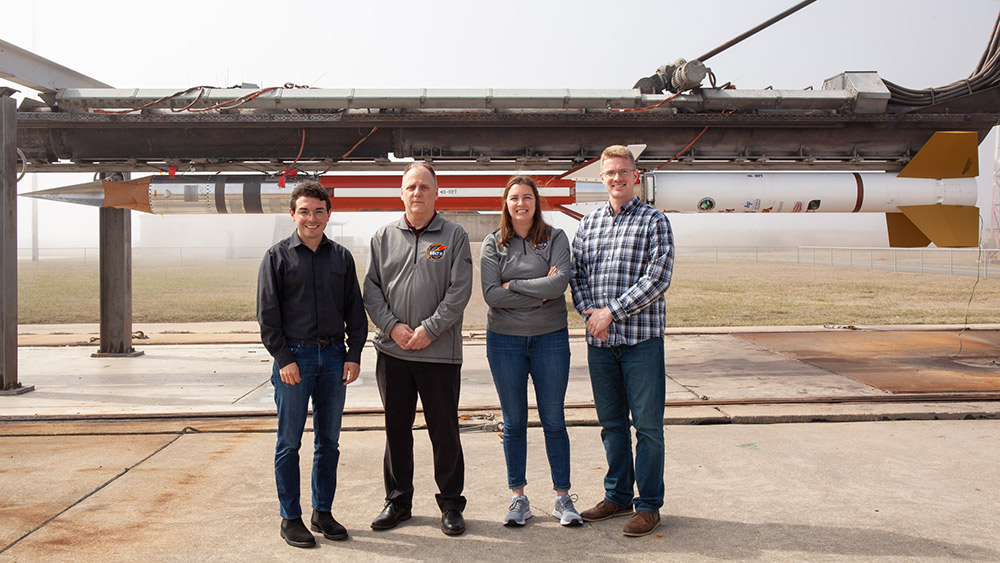 Three graduate students standing with Dr. Rodney Bowersox in front of the BOLT II sounding rocket.