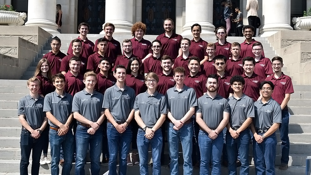 Texas A&amp;M University SAE design team students wearing maroon and gray polos posed for a photo on the steps of the administration building.