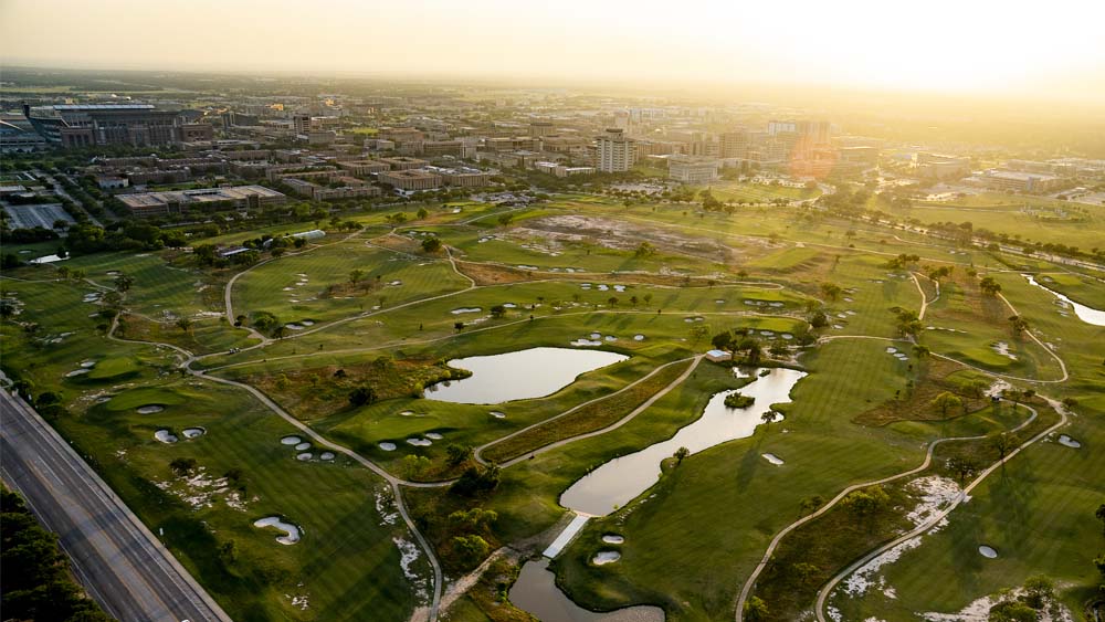 An aerial view of a green space with two lakes and a rising sun on the horizon.