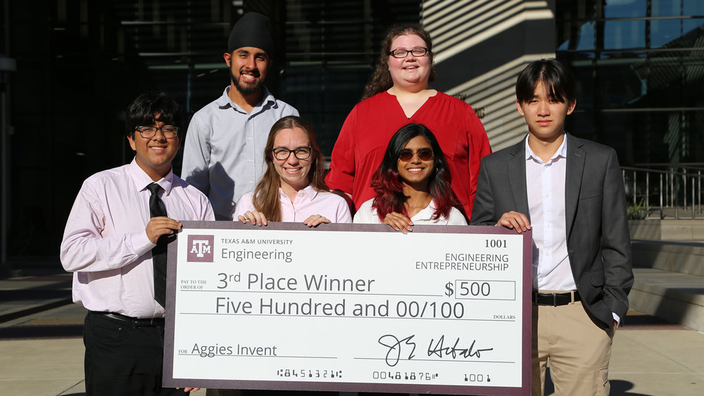 Six members of third-place team, Illuminate, holding a large sign representing a check awarded to them for $500.