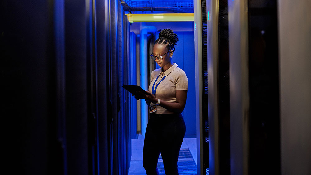 Female engineer using a digital tablet while working in a data center server room.