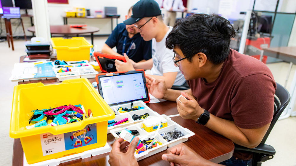 In a classroom, workshop participants interact with the robotics programming interface with Lego robotics kits on a table.