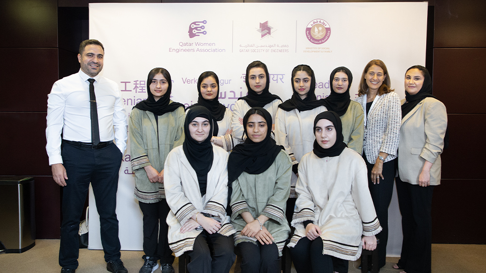 Dr. Mohamed Gharib stands with the Afghan Dreamers team. In the background, sponsors are displayed on a backdrop: Qatar Women Engineers Association, Qatar Society of Engineers, Ministry of Social Development &amp; Family.