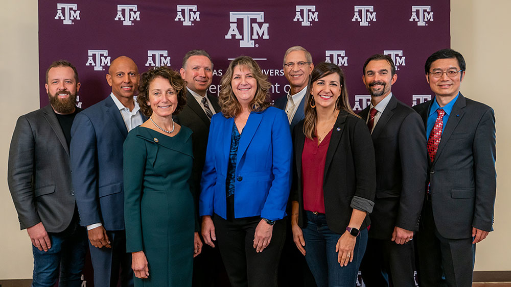 Dr. Mike McShane, department head, and symposium speakers in front of a Texas A&M University banner.