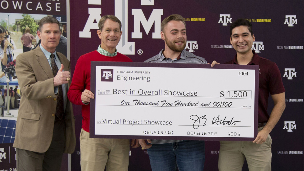 Two faculty and two students stand in front of a maroon backdrop. They are holding an oversized check for $1,500 for winning the Virtual Project Showcase.