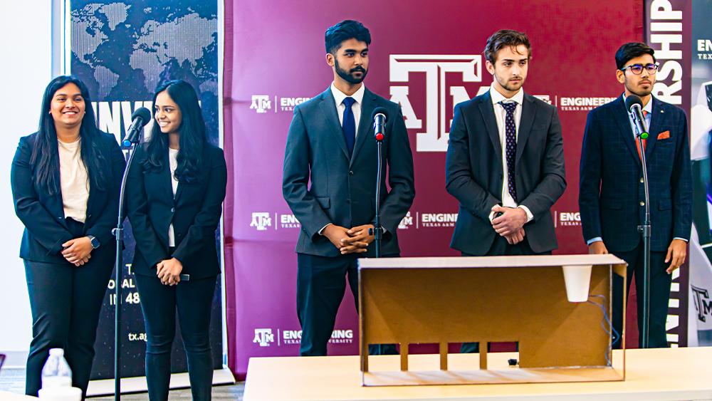 The Innovation Nation team stands behind a cardboard porotype of their project with microphones in front of them.