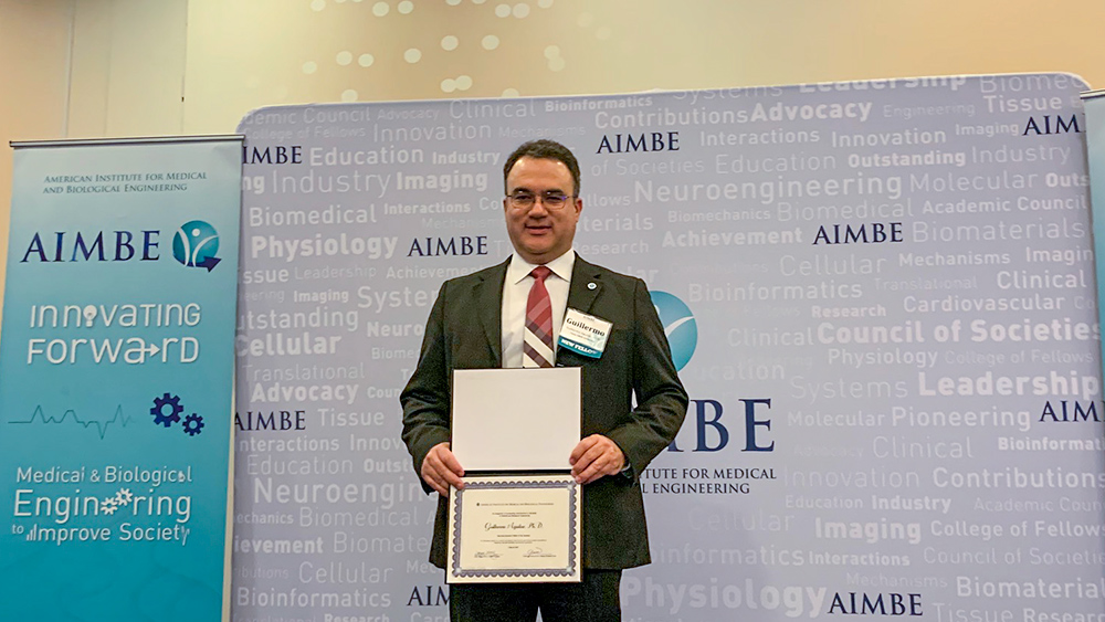 Guillermo Aguilar posing with a certificate in front of an American Institute for Medical and Biological Engineering backdrop.
