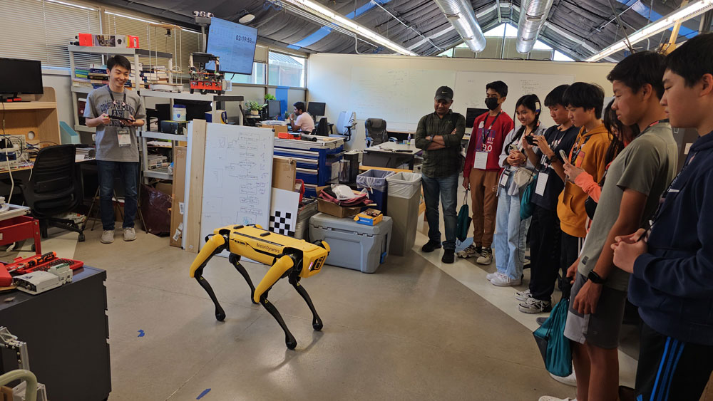 A computer science and engineering student operating a yellow Boston Dynamics robot dog for a group of grad school students.