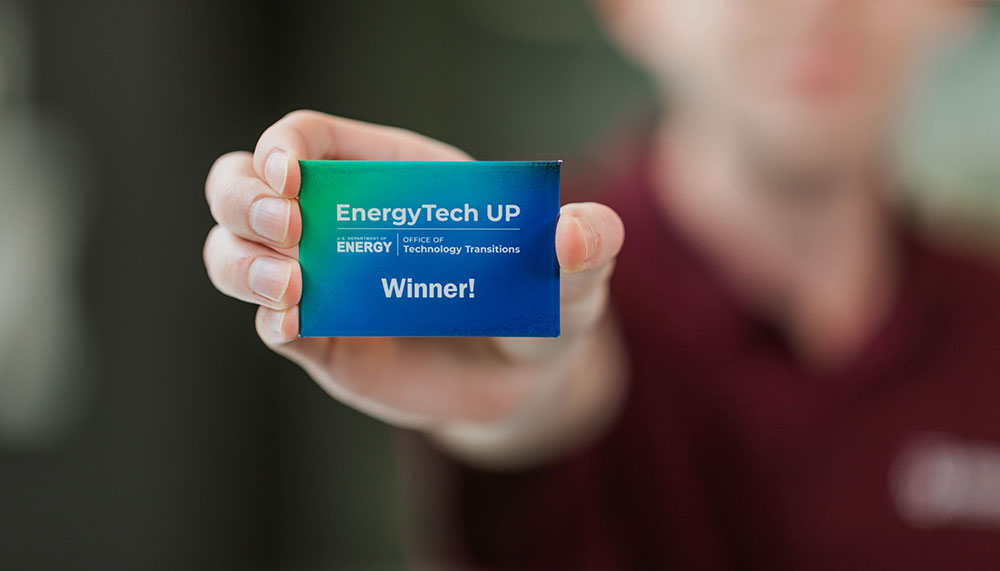 hand holding blue-green card that says EnergyTech UP Winner!