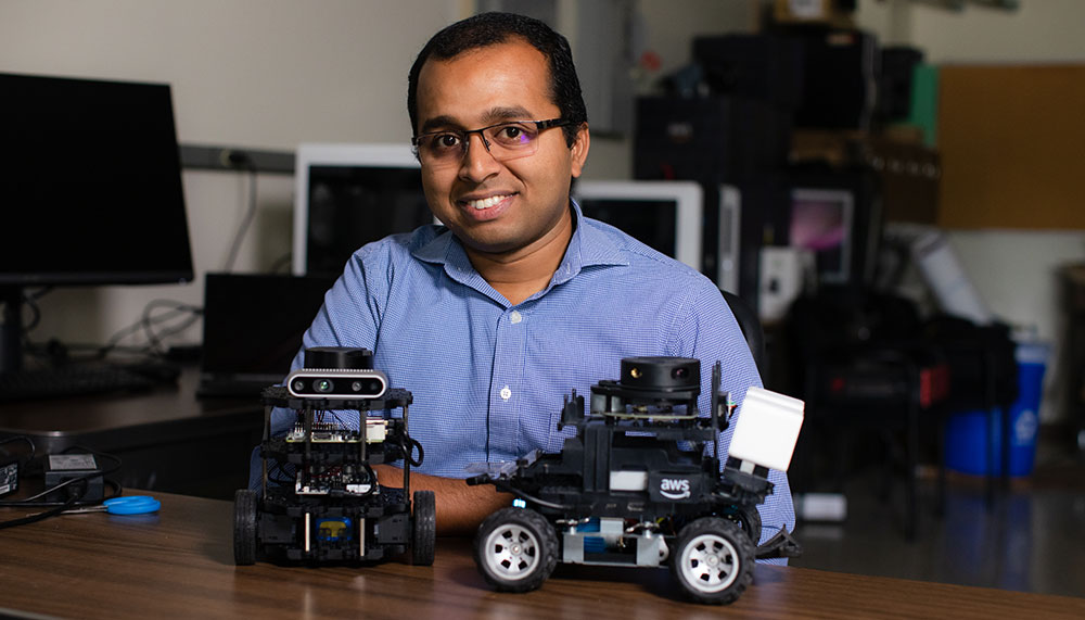 Dr. Dileep Kalathil sitting at desk with tiny autonomous vehicles
