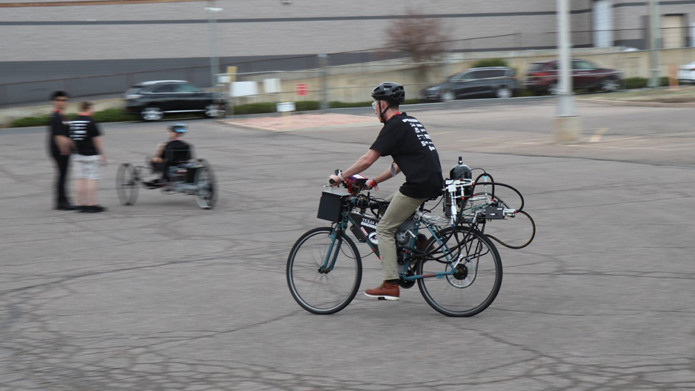 Dalton Yingst riding a bicycle with hoses and a tank connected to the bike.