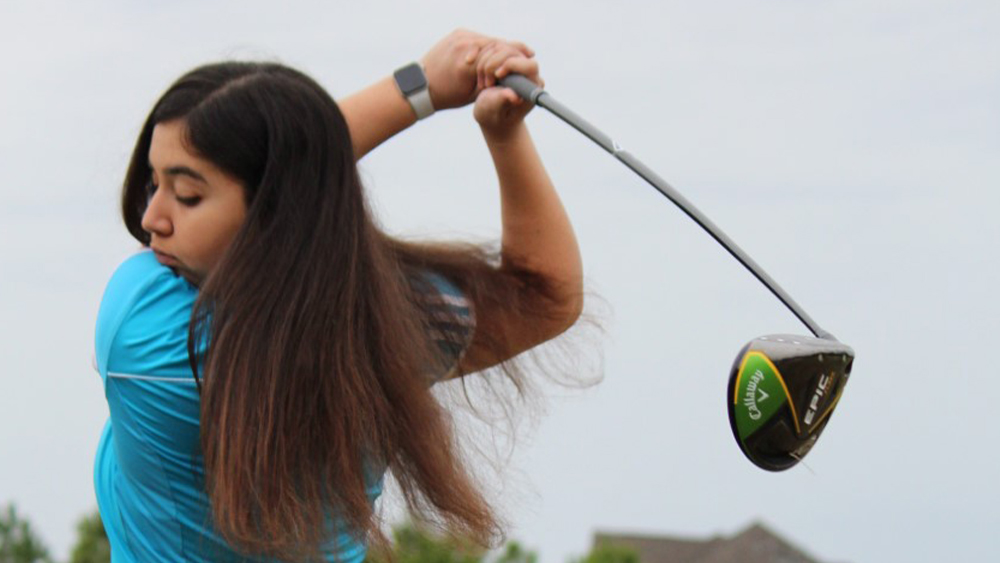 Katie Calderon grips a golf club that she has raised around her and behind her back.