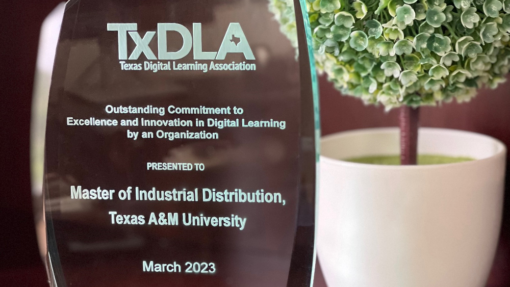 The TxDLA award, with an artificial plant in the background. Award reads: TxDLA Texas Digital Learning Association, Outstanding Commitment to Excellence and Innovation in Digital Learning by an Organization, presented to Master of Industrial Distribution, Texas A&M University, March 2023.