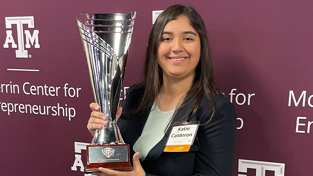Katie Calderon holds a trophy in front of a backdrop with the Texas A&amp;M University logo that reads: McFerrin Center for Entrepreneurship.