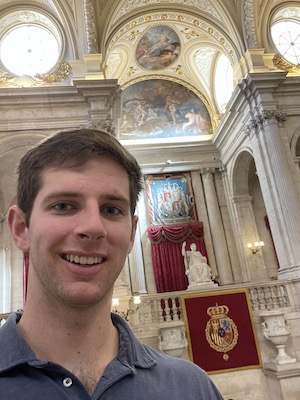 Austin Kees stands in the Royal Palace of Madrid. Behind him is a statue of a man holding a scepter on a throne.