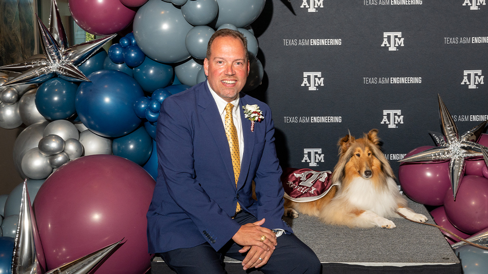 Surrounded by balloons, Dan Tinker sits next to Reveille X in front of a backdrop with the Texas A&amp;M University and Texas A&amp;M Engineering logos.