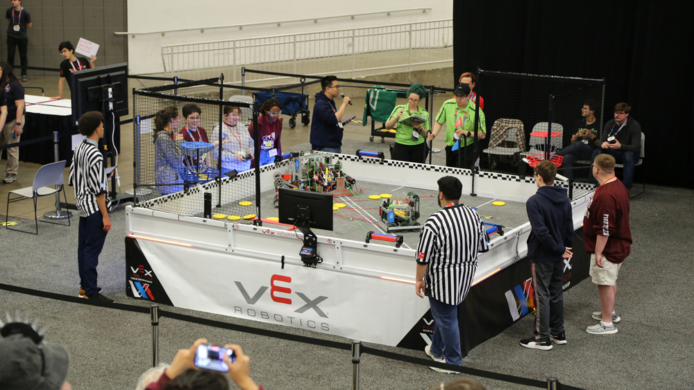 Students surround an arena at the competition where their robots are trying to complete tasks.