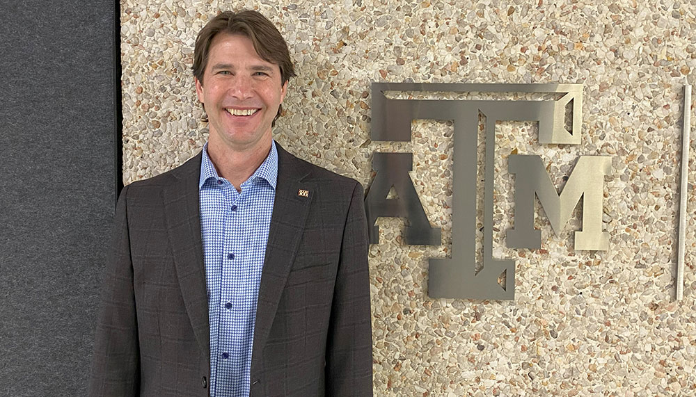 Paul Deere standing in front of a wall with Texas A&amp;M logo