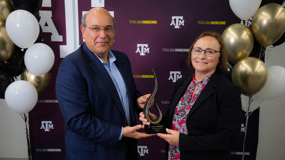 Standing in front of a backdrop with a Texas A&amp;M logo, Dr. Dimitris Lagoudas hands an award to Susan Borsh.