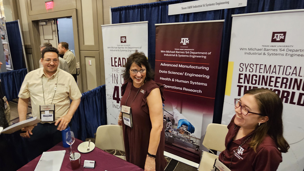From left, Dr. Erick Moreno-Centeno, Cheryl Kocman and Katelyn Wilson stand at a booth table covered with a maroon tablecloth. Behind them are several banners with information about the department.