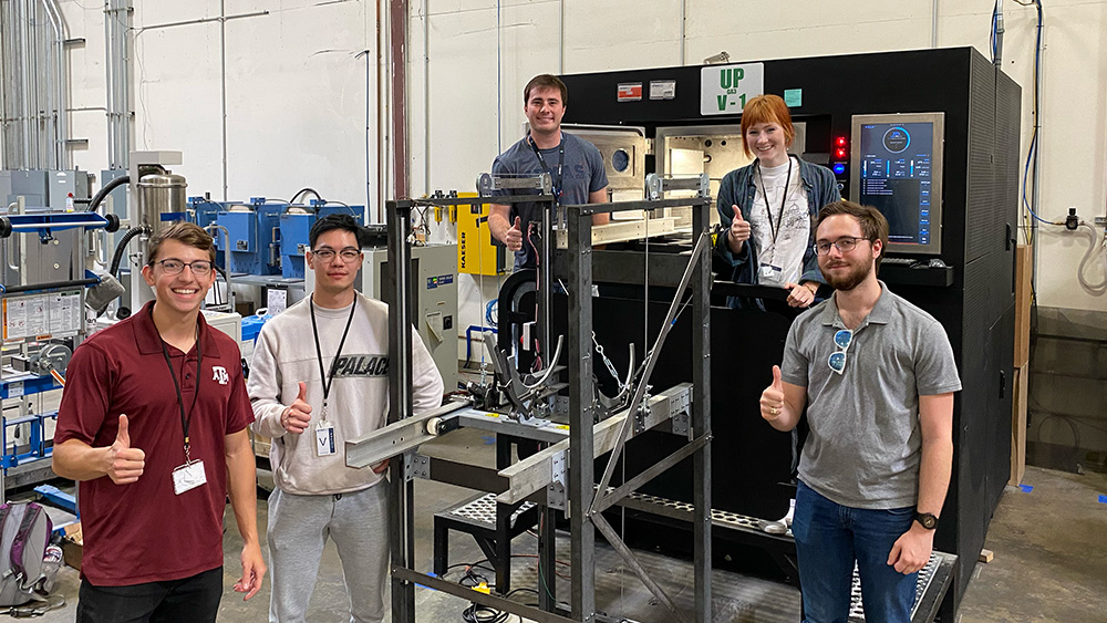 Five mechanical engineering team members posing with their prototype in a test area.
