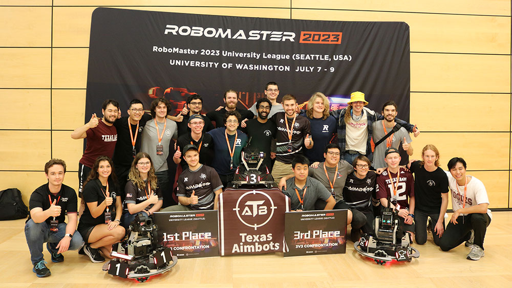 The winning RoboMasters team of students posing for a group photo in front of the Robomaster 2023 competition banner that says RoboMaster 2023 University League (Seattle, USA) University of Washington July 7-9