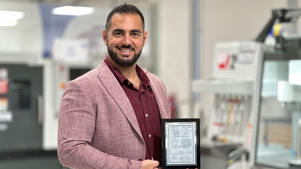 Moustafa Raslan stands in a lab in business attire holding a framed patent. 